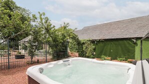 A hot tub in a backyard with a brick wall, green artificial grass, and a fence. - Marshill Farm House (Lanark)