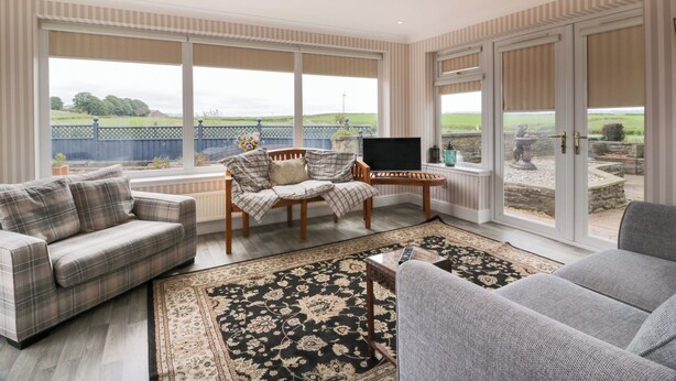 A spacious living room with a large window, a sofa, a chair, and a small table. - Marshill Farm House (Lanark)