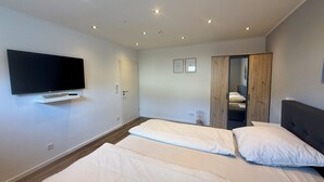 Una habitación de hotel moderna con dos camas, un televisor de pantalla plana y un armario de madera.