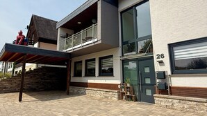 Una casa moderna de dos pisos con balcón, ventanas amplias y una puerta de garaje marcada con el número 26.