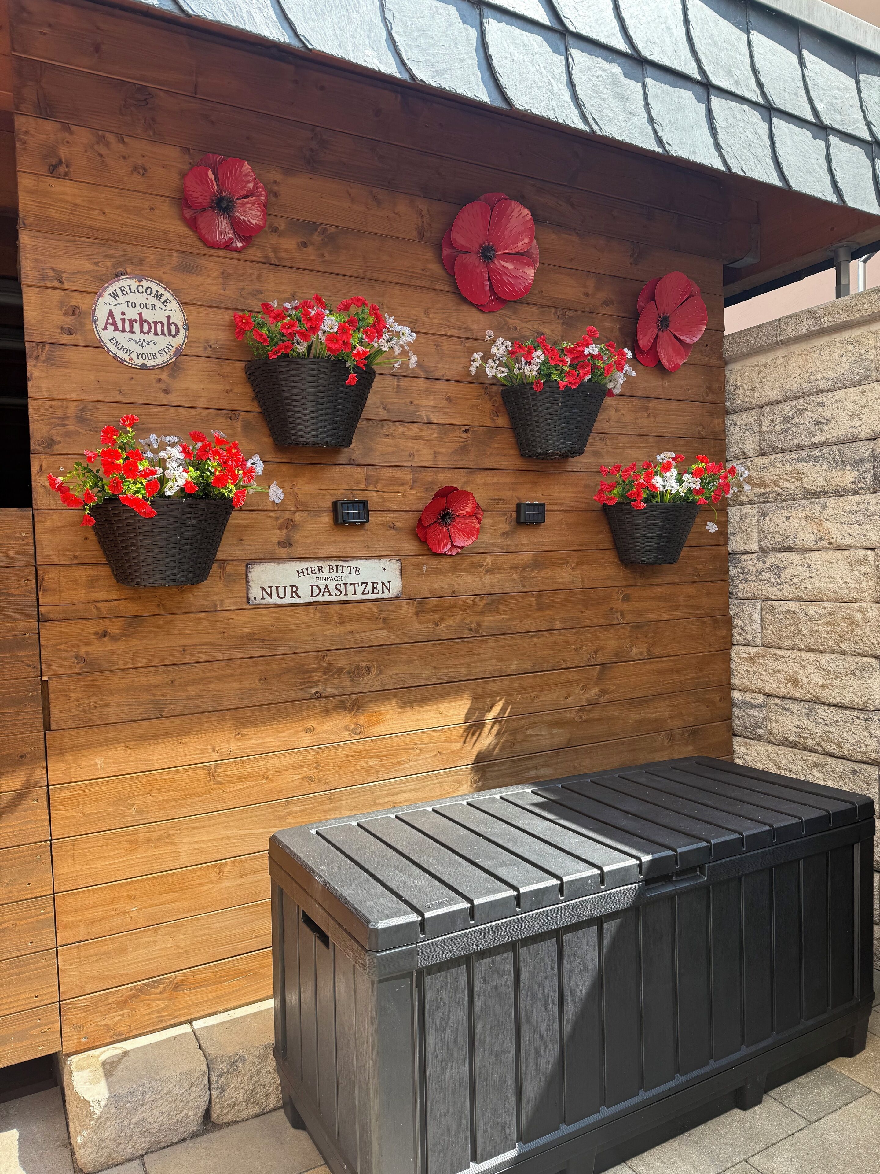 Una pared de madera con macetas de flores y un letrero que dice "Welcome to our Airbnb".