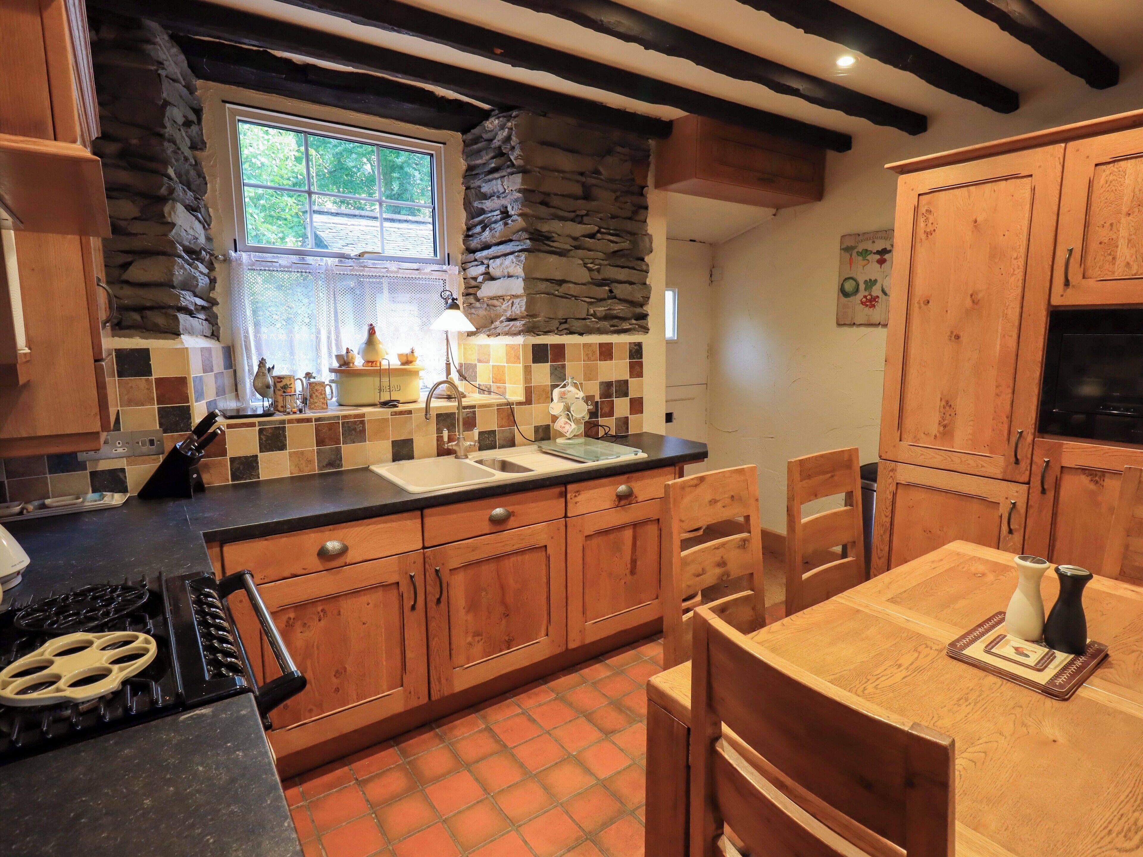 A kitchen with wooden cabinets, a stone accent wall, a tiled backsplash, and a window with a view of greenery.
