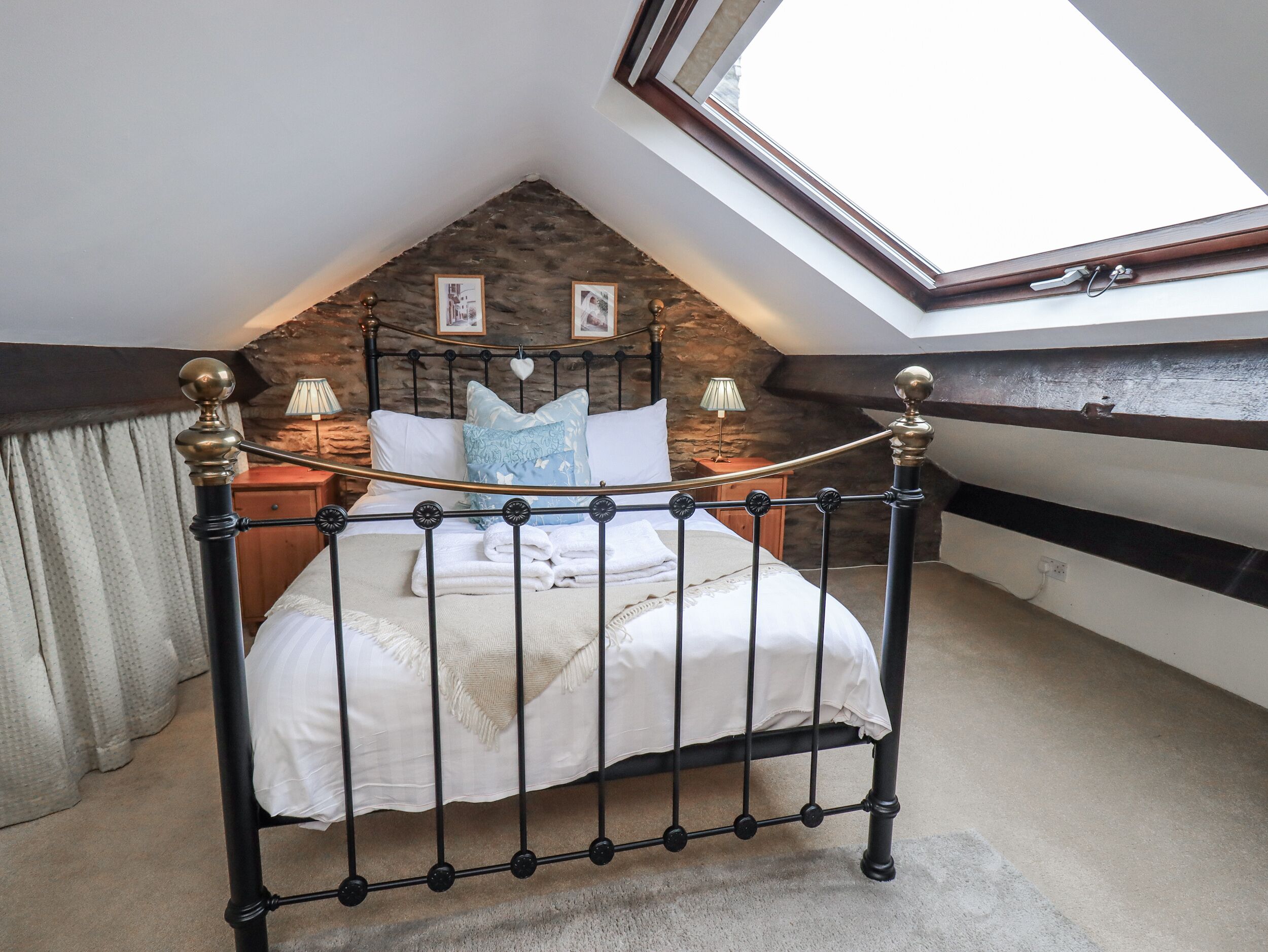 A bedroom with a sloped ceiling, a bed with a metal frame, a wooden headboard, and a skylight.