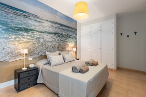 A bedroom with a large ocean mural, a bed with pillows and towels, a nightstand with a lamp, and a wardrobe. - Famara Views III by Escape Home (Famara)