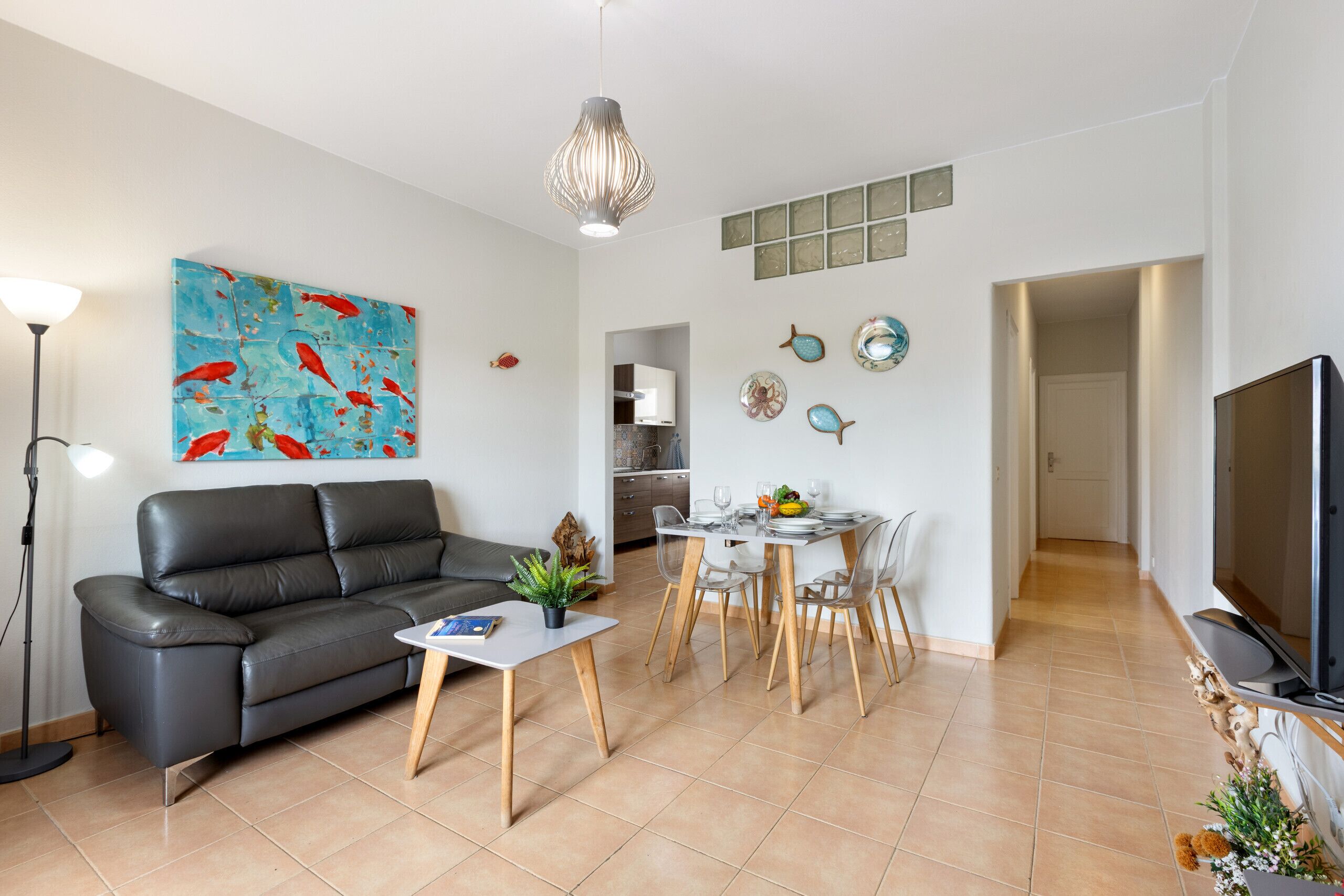Een moderne woonkamer met een zwarte leren bank, een eettafel met stoelen, een televisie en een groot abstract schilderij aan de muur.