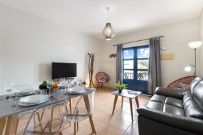 A modern living room with a sofa, dining table, chairs, a TV, and a balcony with a view.