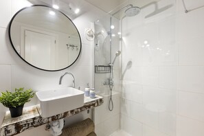 A bathroom with a white sink, a round mirror, a shower with a handheld showerhead, and a towel rack.