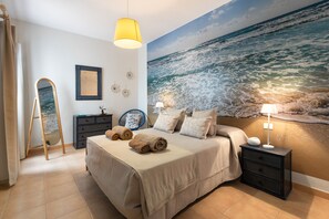A bedroom with a bed, a nightstand, a lamp, a mirror, and a wall mural of the ocean. - Famara Views III by Escape Home (Famara)