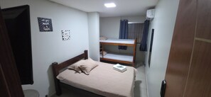 A small, compact room with a single bed, a bunk bed, a toilet, and a wall-mounted air conditioner. - Hangar House Hostel (Belém)