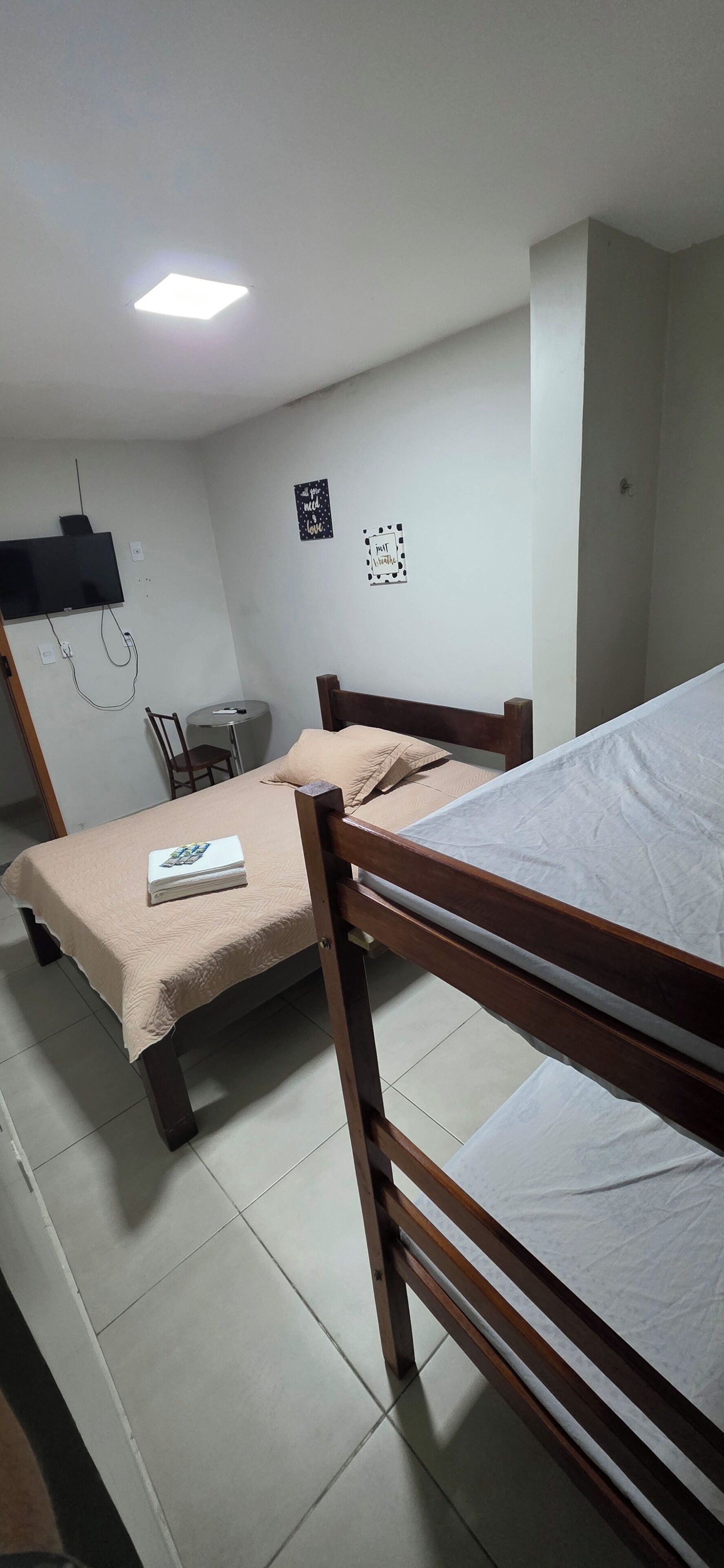 Una habitación con dos literas de madera, una mesita, una silla, un televisor montado en la pared y una lámpara en el techo.