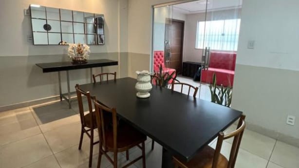 A dining area with a black table and wooden chairs, a small side table with a vase, and a large mirror on the wall. - Hangar House Hostel (Belém)