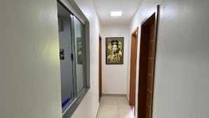 A narrow hallway with white walls and tiled flooring. There is a framed picture on the wall and a door on the right. - Hangar House Hostel (Belém)