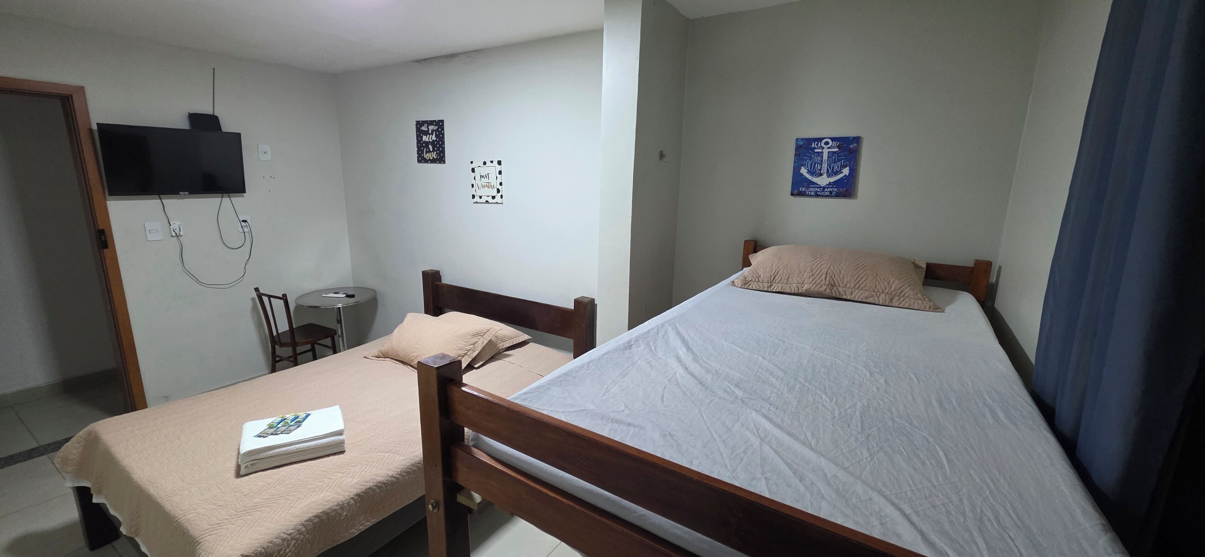 Un dormitorio con cama, mesita de noche, silla y televisor instalado en la pared.