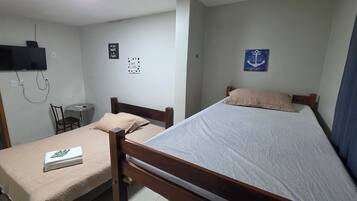 Un dormitorio con cama, mesita de noche, silla y televisor instalado en la pared.