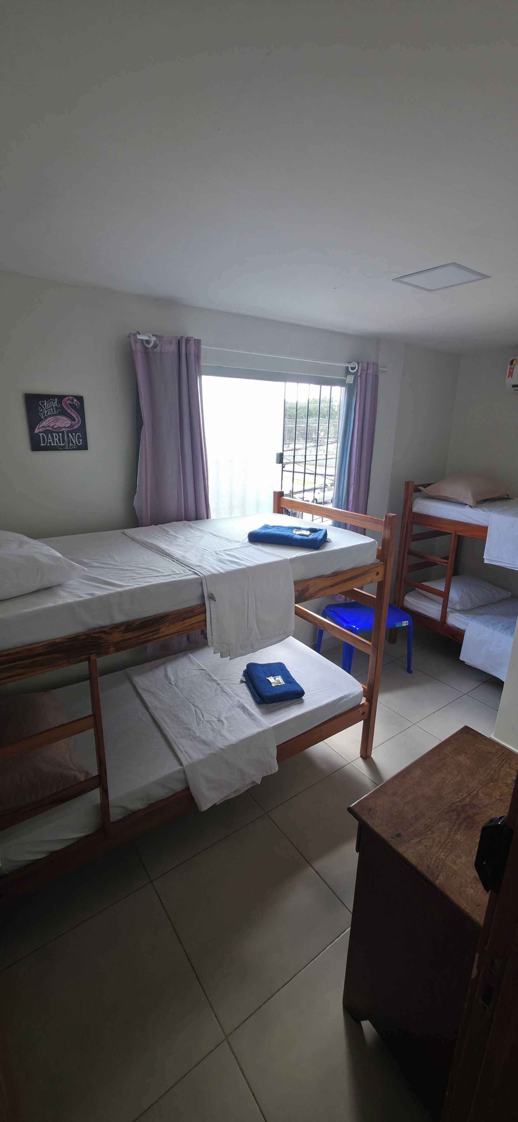 A dormitory room with bunk beds, a desk, a chair, and a window with curtains.