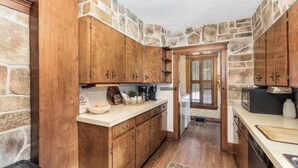 A kitchen with wooden cabinets, a stone wall, and a view into another room.