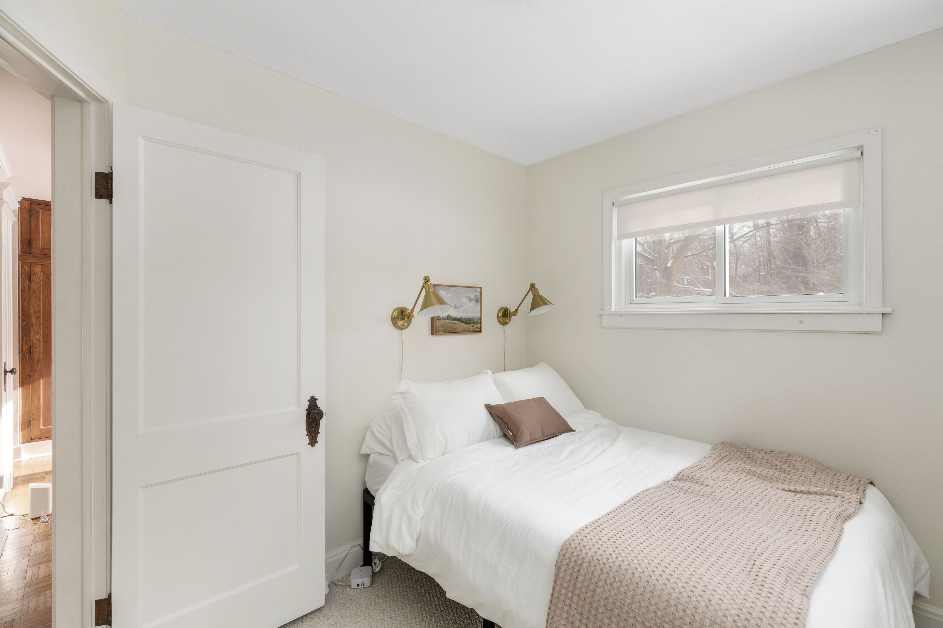 Une chambre à coucher avec un lit, une fenêtre, une porte et une lampe fixée au mur.