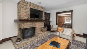 A living room with a stone fireplace, a flat-screen TV mounted above it, and a comfortable seating area with a sofa and armchairs.