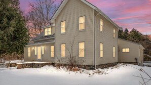 A two-story house with a stone foundation and a sloped roof, surrounded by snow.