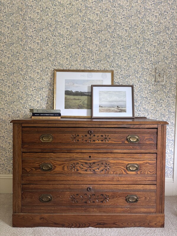 A wooden dresser with four drawers, each featuring a metal handle. On top of the dresser, there are two framed pictures and a stack of books. - Historic 1896 Farmhouse on 13 Acres, Sleeps 12, 7 Min to Pine Knob (Village of Clarkston)