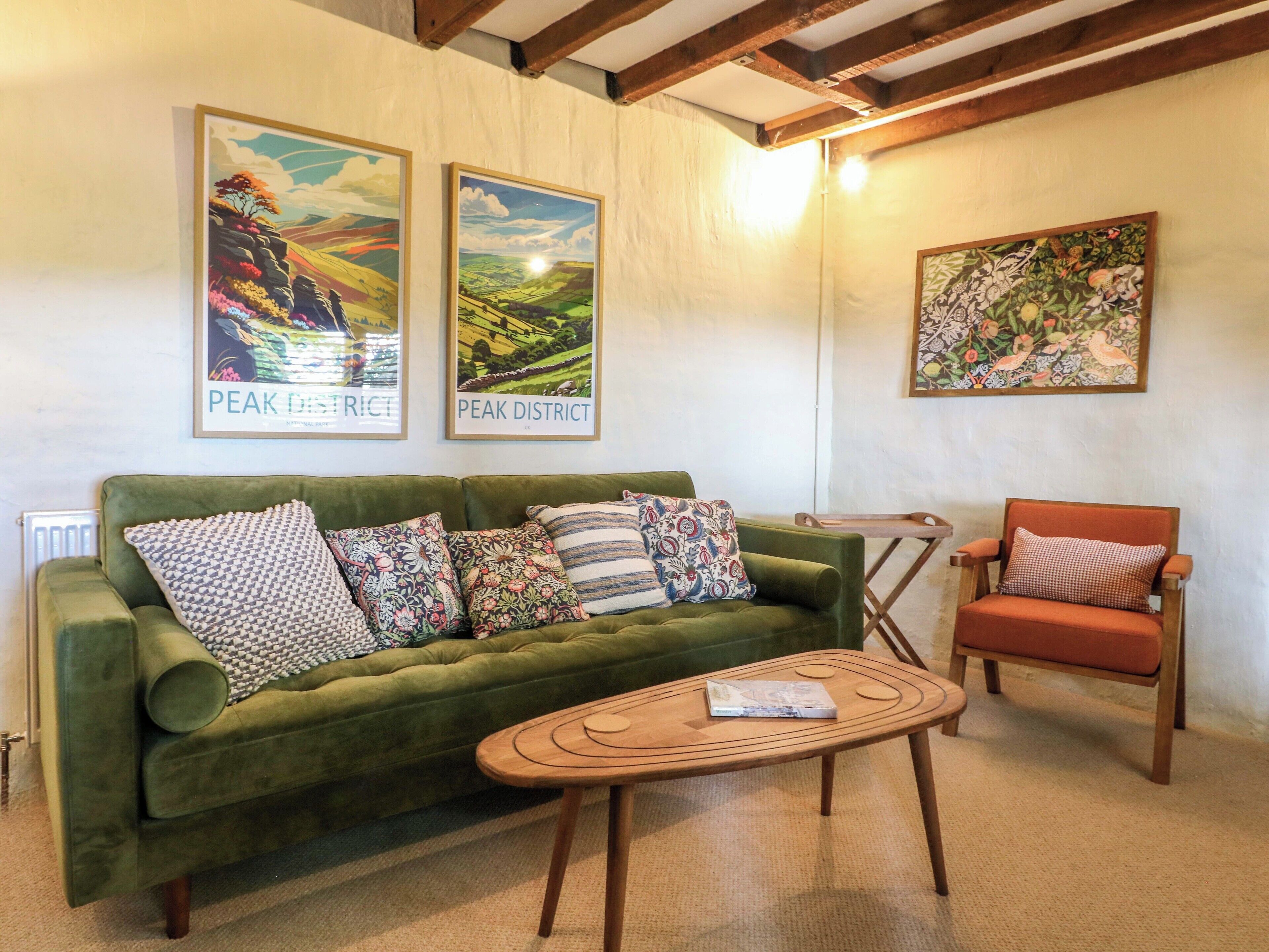 A green sofa with patterned cushions, a wooden coffee table, and a wooden chair with a cushion. Two framed landscape paintings are on the wall.