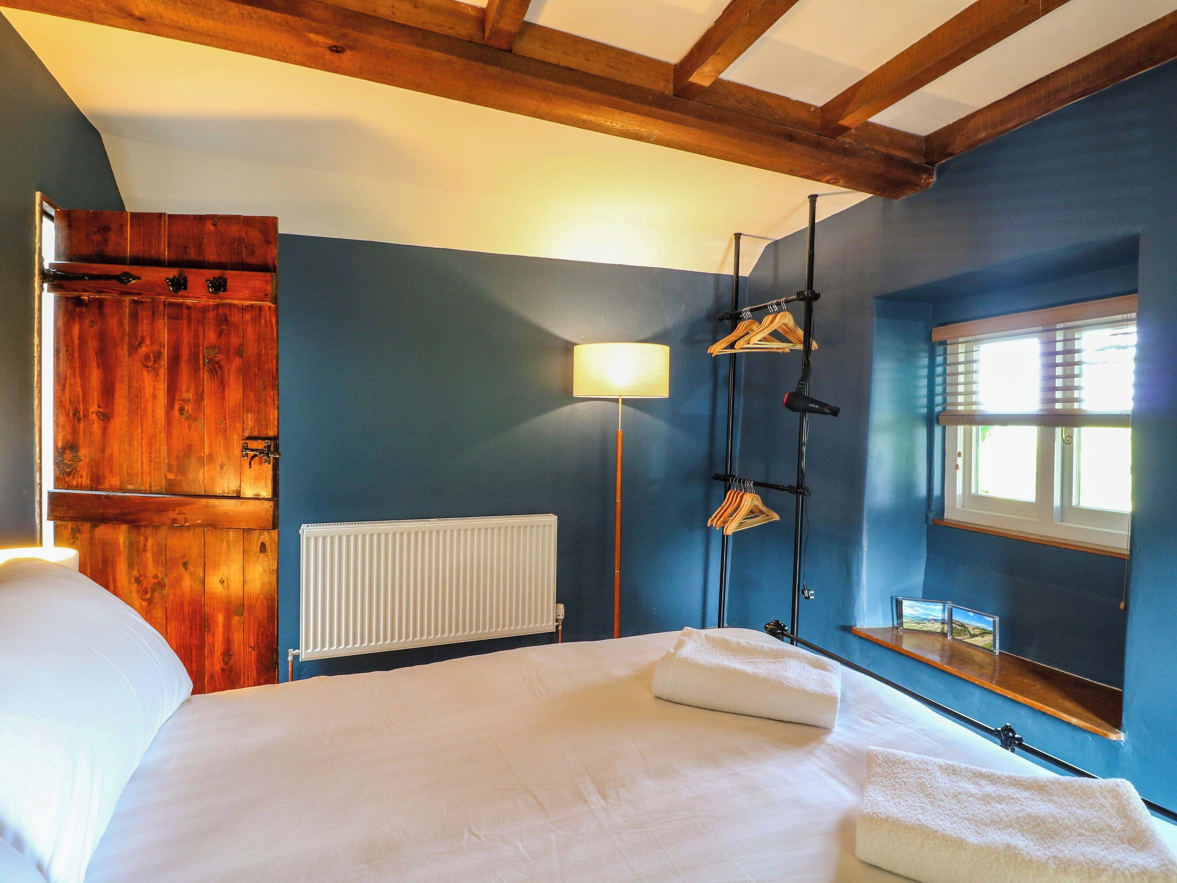 Un dormitorio con cama, armario de madera, radiador, lámpara y ventana con persianas.
