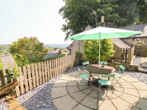 A patio with a round table and chairs, a green umbrella, and a view of a village in the background.