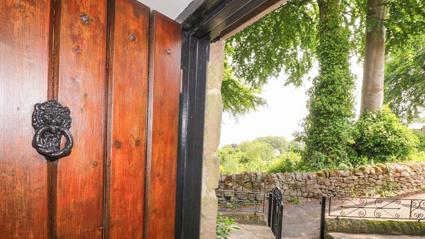 Una puerta de madera con un aldabón de metal, que da a un área empedrada de piedra con un muro de piedra y barandilla de metal.