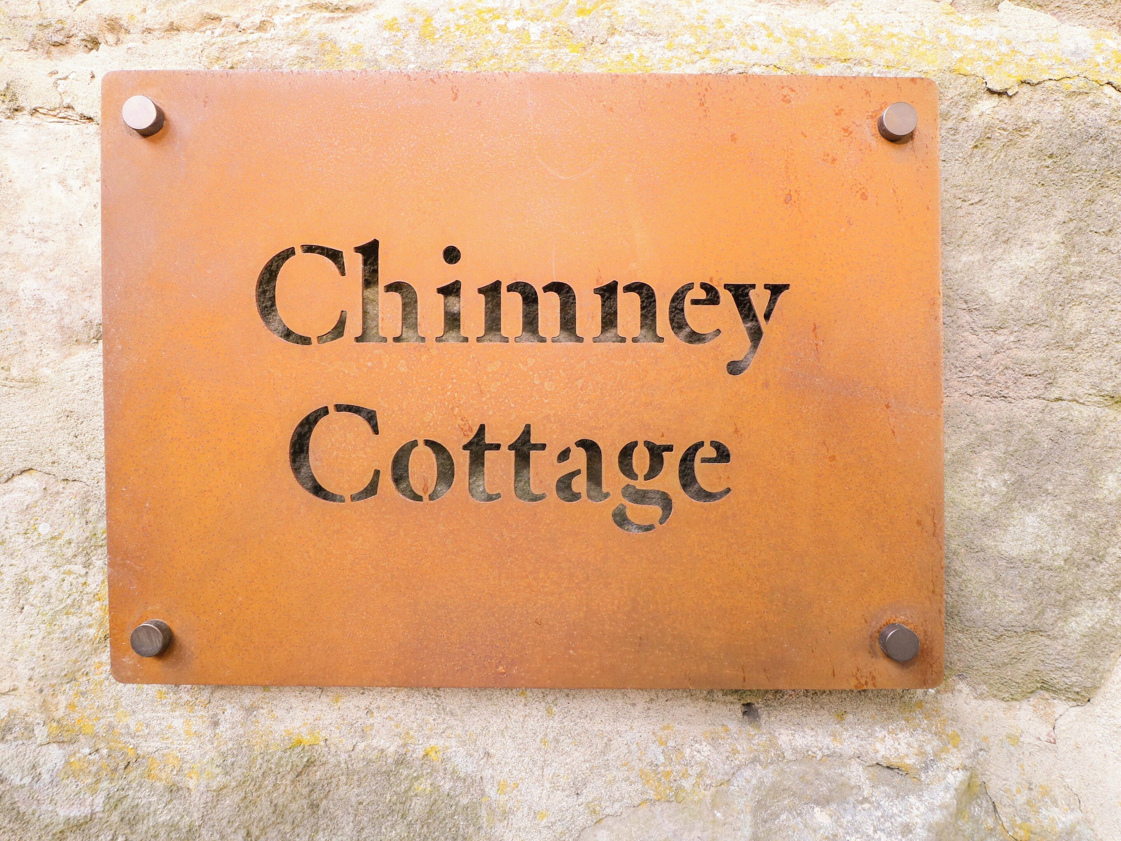 Een metalen plaquette met de tekst 'Chimney Cottage' bevestigd aan een muur.
