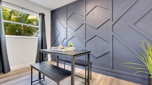 Une chambre moderne avec un panneau mural géométrique de couleur sombre, un plancher en bois, une petite table avec un plateau et une plante en pot.
