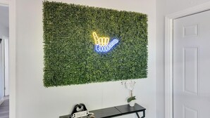 Un mur orné d’un panneau néon sur lequel on peut lire « Good Vibes », et une petite plante en pot posée sur une console noire.