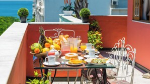 A table set with breakfast items, including fruits, pastries, and beverages, on a balcony with a view of the ocean. - The Coral Penthouse - 4 Bedrooms (Rio de Janeiro)