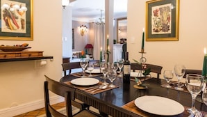A dining area with a wooden table set for six, surrounded by chairs. There are framed botanical prints on the walls, a chandelier, and a candle holder with candles. - The Coral Penthouse - 4 Bedrooms (Rio de Janeiro)