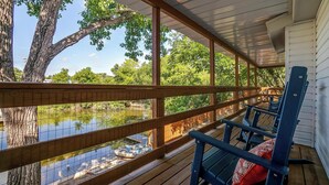 Eine Holzterrasse mit Blick auf einen Teich und Bäume, sowie blaue Stühle mit roten Kissen.