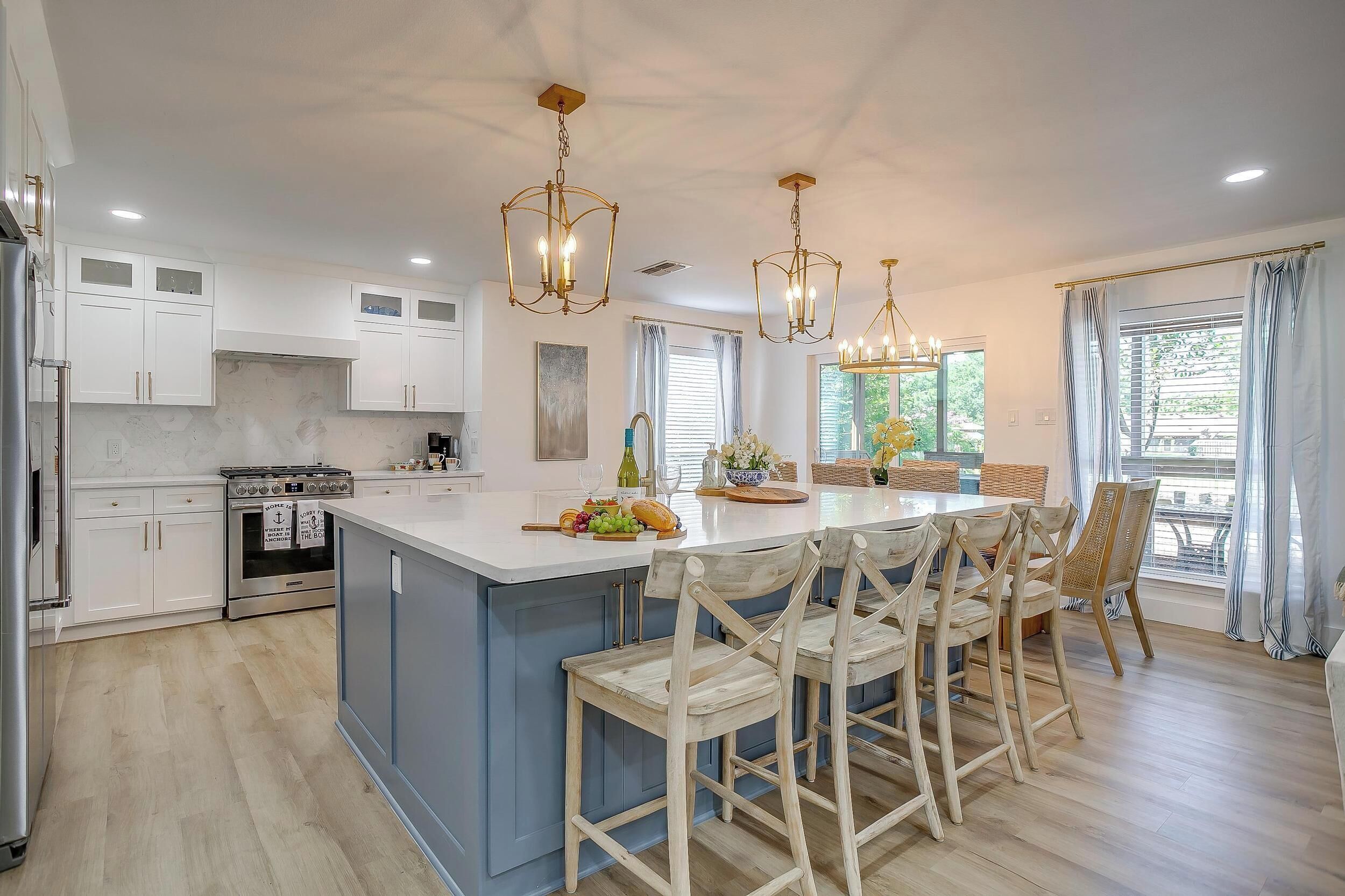 Une cuisine moderne avec des meubles blancs, un îlot central doté de tabourets et des luminaires suspendus.
