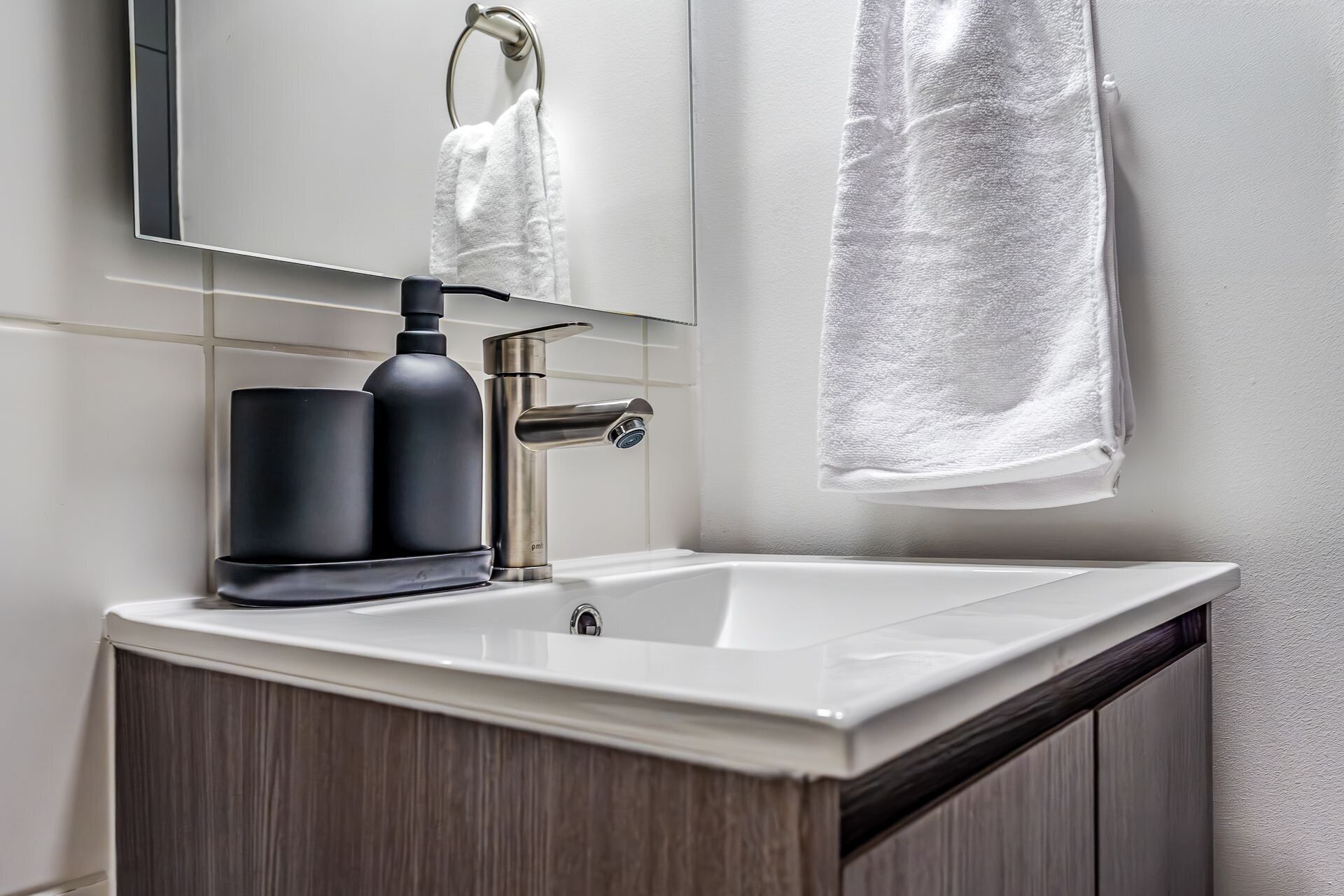 Un baño moderno con un lavamanos blanco, un dispensador de jabón negro y un grifo plateado.