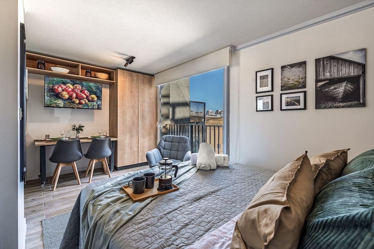 Ein modernes Schlafzimmer mit einem großen Bett, einem Schreibtisch mit Stühlen und einem Balkon mit Blick auf die Stadt.