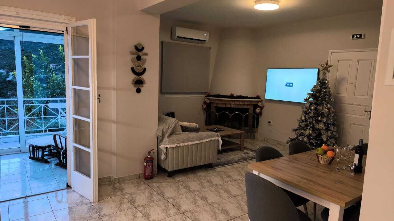 A living room with a fireplace, a Christmas tree, a dining table with chairs, and a sliding glass door leading to a balcony.