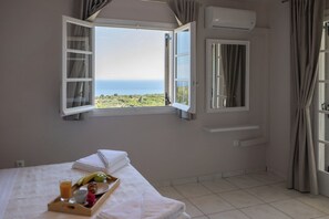 A hotel room with a bed, a tray with breakfast items, a window with a view of the sea, and an air conditioning unit. - ADRIANA'S House KARDAMYLI PROSILIO (Unknown)