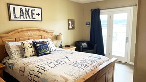 A bedroom with a bed, a nightstand, a chair, and a view of the outdoors.