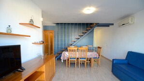 A living room with a TV, wooden furniture, a blue sofa, a staircase, and a tiled wall. - Apartment in Spain Near Sandy Beach (Torroella de Montgrí)