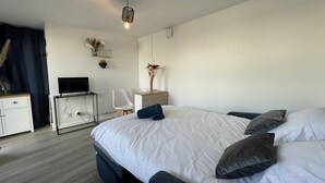 A modern bedroom with a large bed, a desk with a flat-screen TV, a chair, and a decorative vase.
