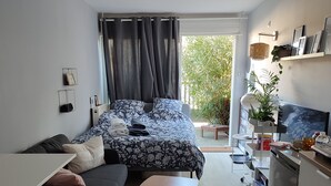 A compact living space with a bed, a small dining table, a kitchenette, and a view of greenery outside. - Studio good vibes only (Toulouse)