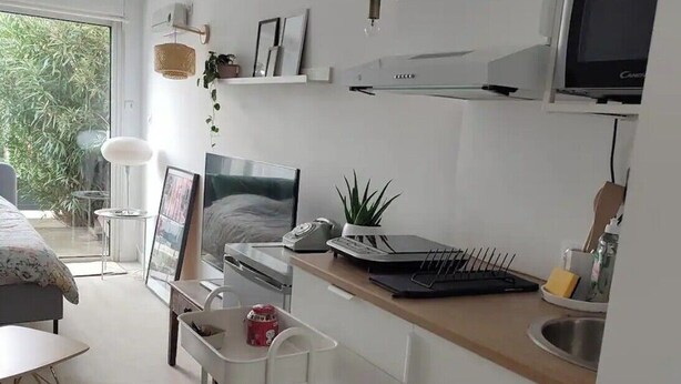A modern kitchen with white cabinetry, a microwave, a sink, and a small dining area with a table and chairs. - Studio good vibes only (Toulouse)