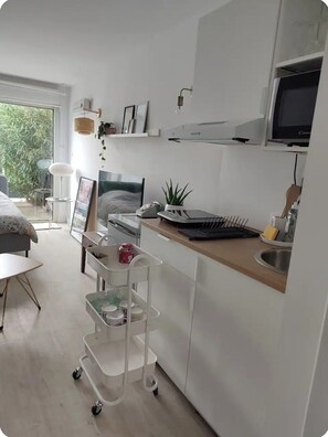A modern kitchen with white cabinetry, a microwave, a sink, and a small dining area with a table and chairs. - Studio good vibes only (Toulouse)