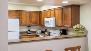 A kitchen with wooden cabinets, a white refrigerator, a microwave, a stove, a blender, a toaster, and a coffee maker.