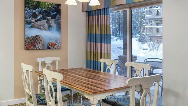 A dining area with a wooden table and white chairs, a painting of a waterfall, and a view of a snowy landscape through large windows.