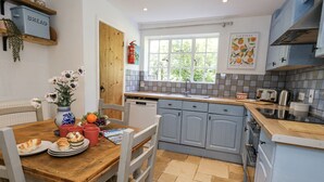 A kitchen with a wooden table, white chairs, a sink, and a window. - Happiness Cottage (Dorchester)