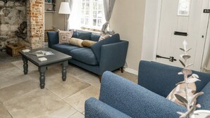 A living room with a blue sofa set, a small table, a fireplace, and a door with a keyhole. - Happiness Cottage (Dorchester)