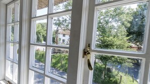 A room with multiple windows, a brass door handle, and a view of a street and greenery outside. - Happiness Cottage (Dorchester)